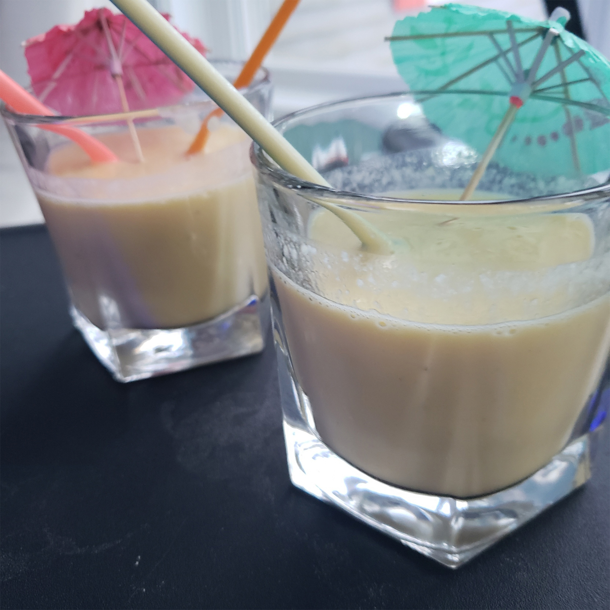 Banana Mango Smoothies in glasses with straws and umbrellas
