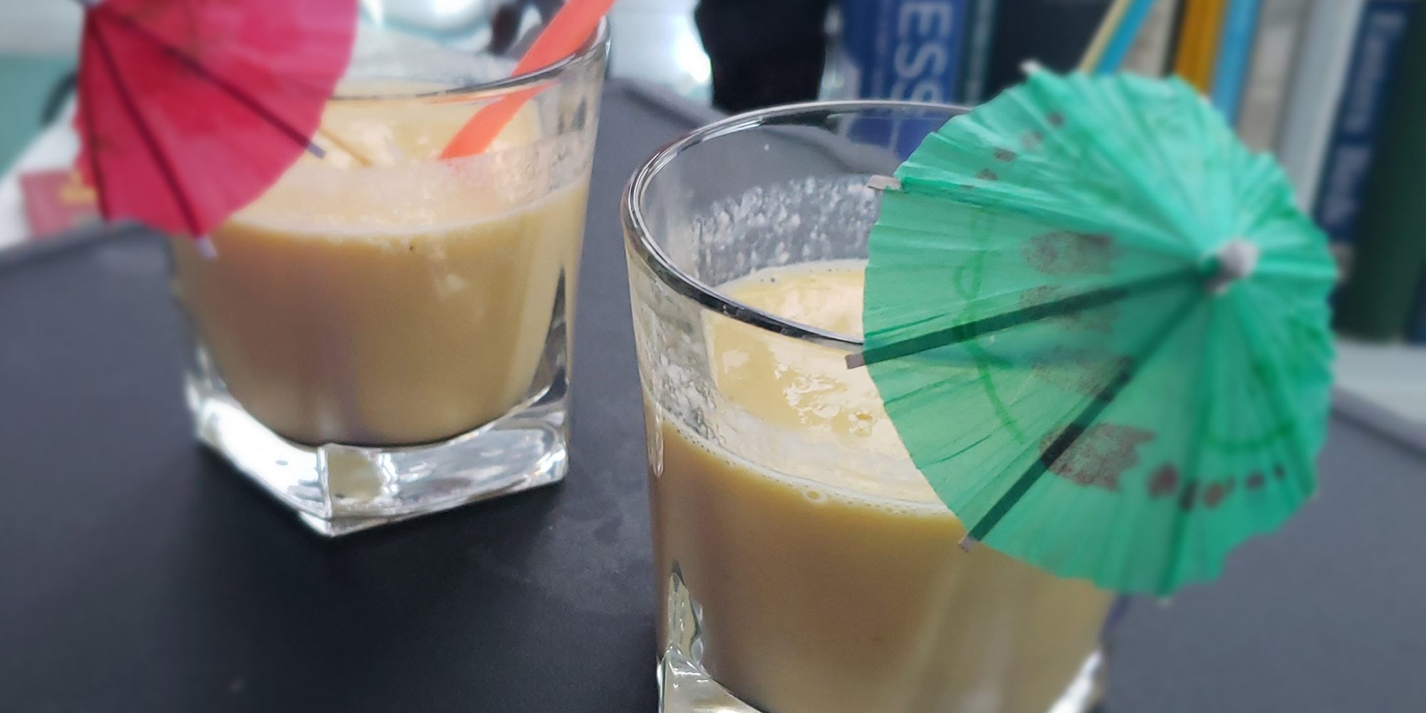 Two glasses with umbrellas and straws filled with smoothie