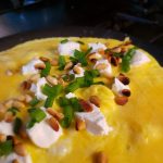 Omelette with feta cheese, green onions, and pine nuts in the skillet