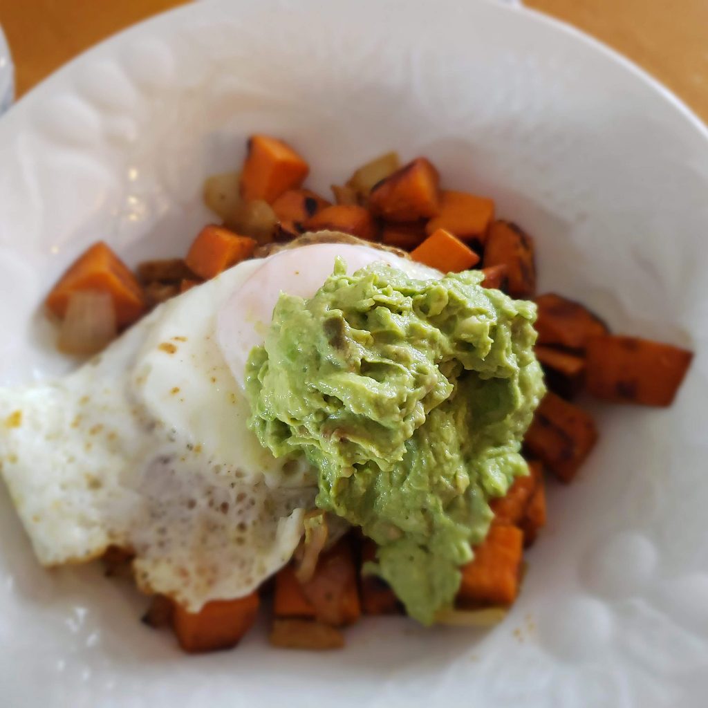 Sweet potato hash with fried egg and avocado aioli on a white plate