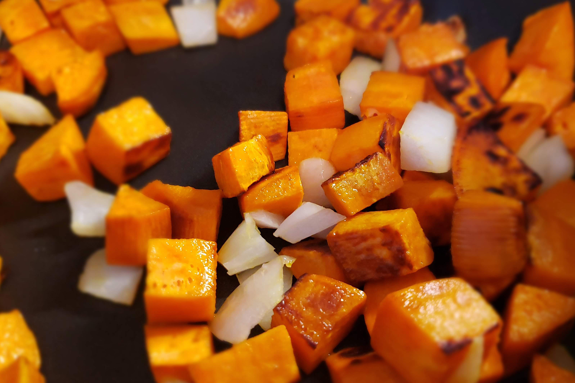 Sweet potato cubes and onions sauteing in skillet
